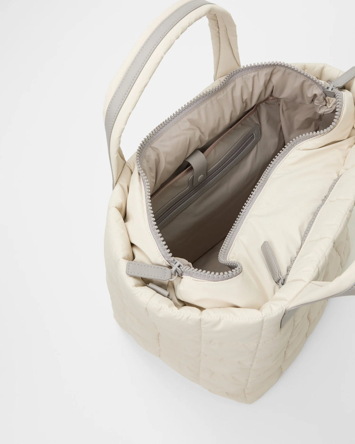 Open Vee Collective Porter Tote Bag Medium in Barely Beige, showing the quilted exterior, top zipper, and interior compartments of the tote bag.