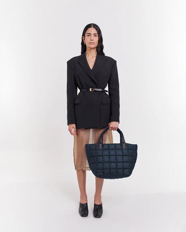 On-body picture of a woman holding the Medium Porter Tote Bag in Dark Navy by Vee Collective, wearing a minimalistic outfit against a clean studio background.