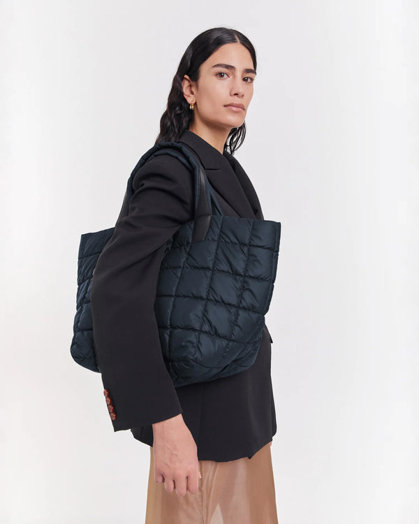 On-body picture of a woman Carrying the Medium Porter Tote Bag in Dark Navy by Vee Collective, wearing a minimalistic outfit against a clean studio background.
