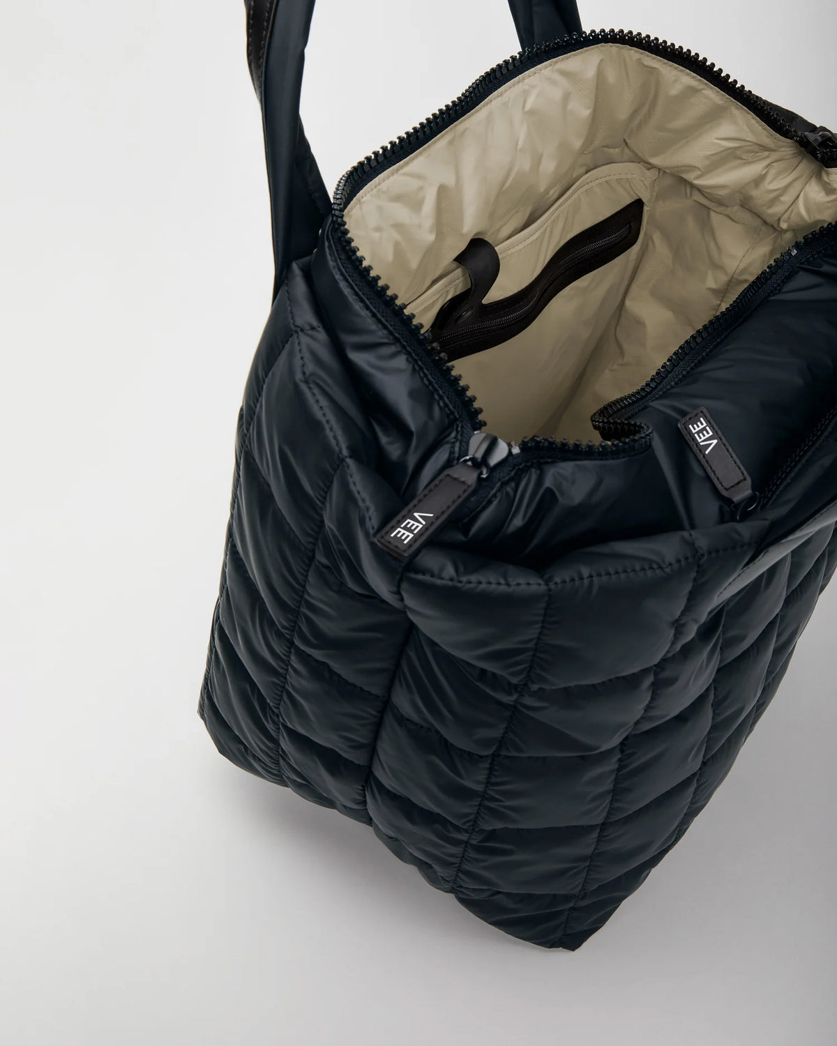 Open Vee Collective Porter Tote Bag Medium in Dark Navy, showing the quilted exterior, top zipper, and interior compartments of the tote bag.
