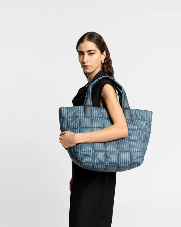 On-body picture of a woman holding the Medium Porter Tote Bag in Pinstripe by Vee Collective, wearing a minimalistic outfit against a clean studio background.