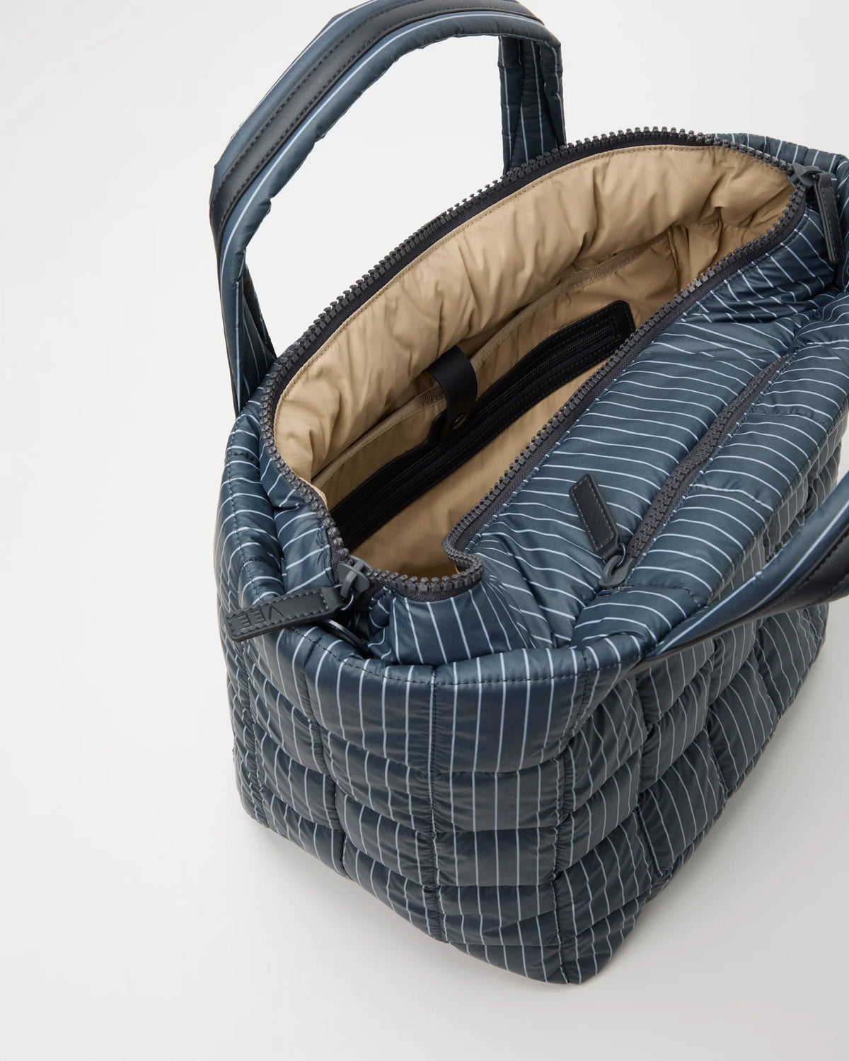 Open Vee Collective Porter Tote Bag Medium in Pinstripe, showing the quilted exterior, top zipper, and interior compartments of the tote bag.