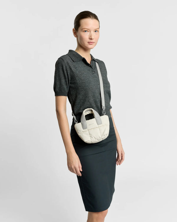 On-body picture of a woman carrying the Micro Porter Tote Bag in Barely Beige by Vee Collective, styled crossbody with the attachable strap, wearing a minimalistic outfit against a clean studio background.