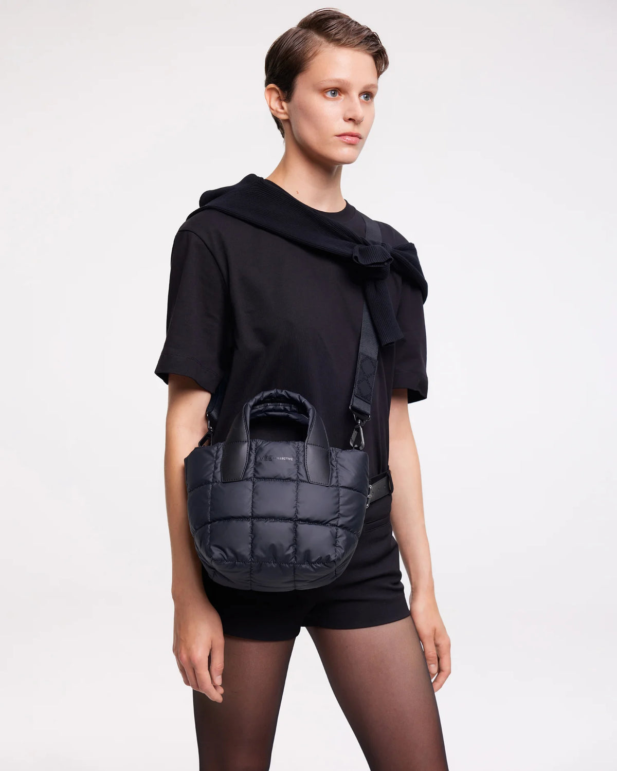 On-body picture of a woman carrying the Mini Porter Tote Bag in Dark Navy by Vee Collective, styled crossbody with the attachable strap, wearing a minimalistic outfit against a clean studio background.