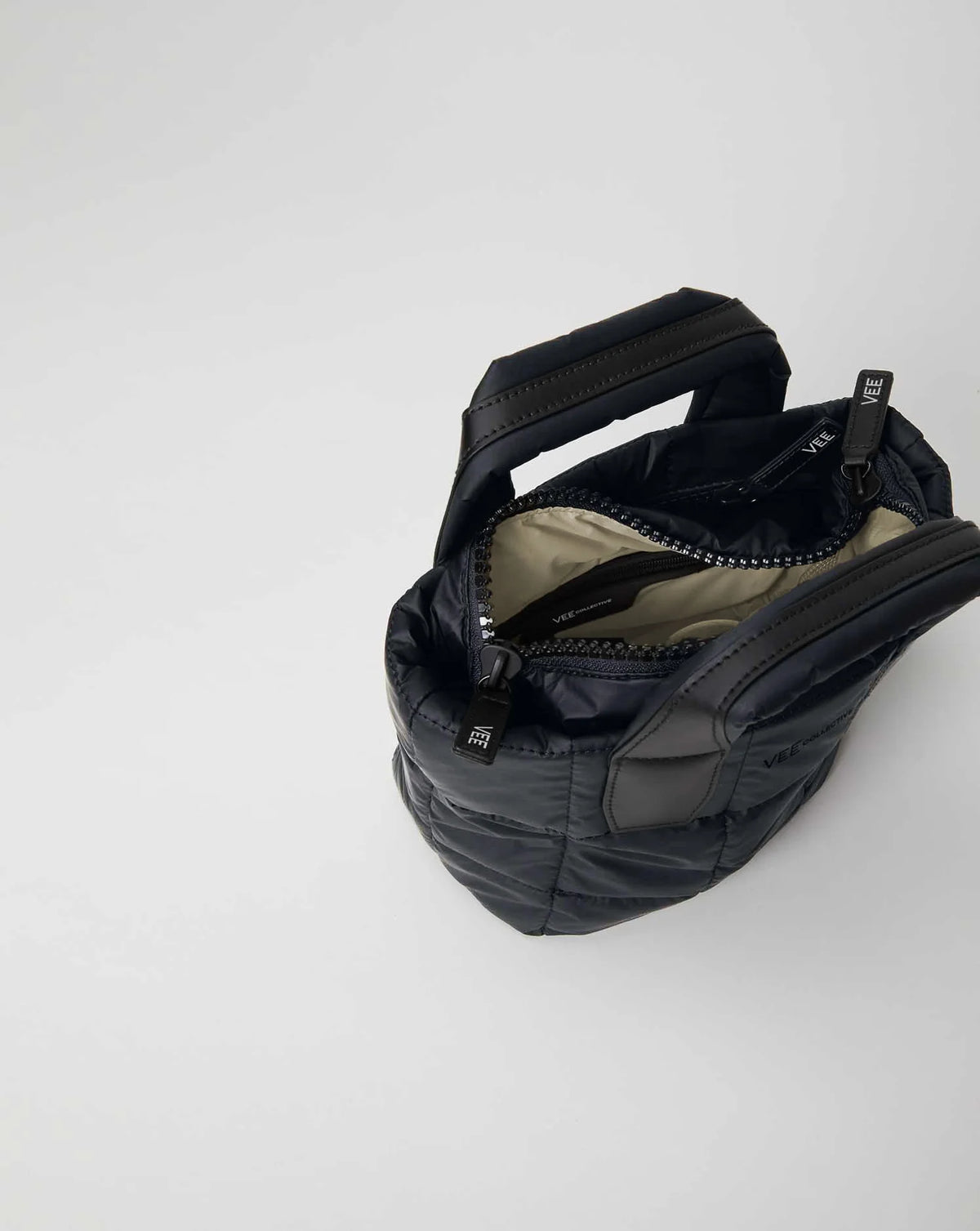 Open Vee Collective Porter Tote Bag Mini in Dark Navy, showing the quilted exterior, top zipper, and interior compartments of the tote bag.