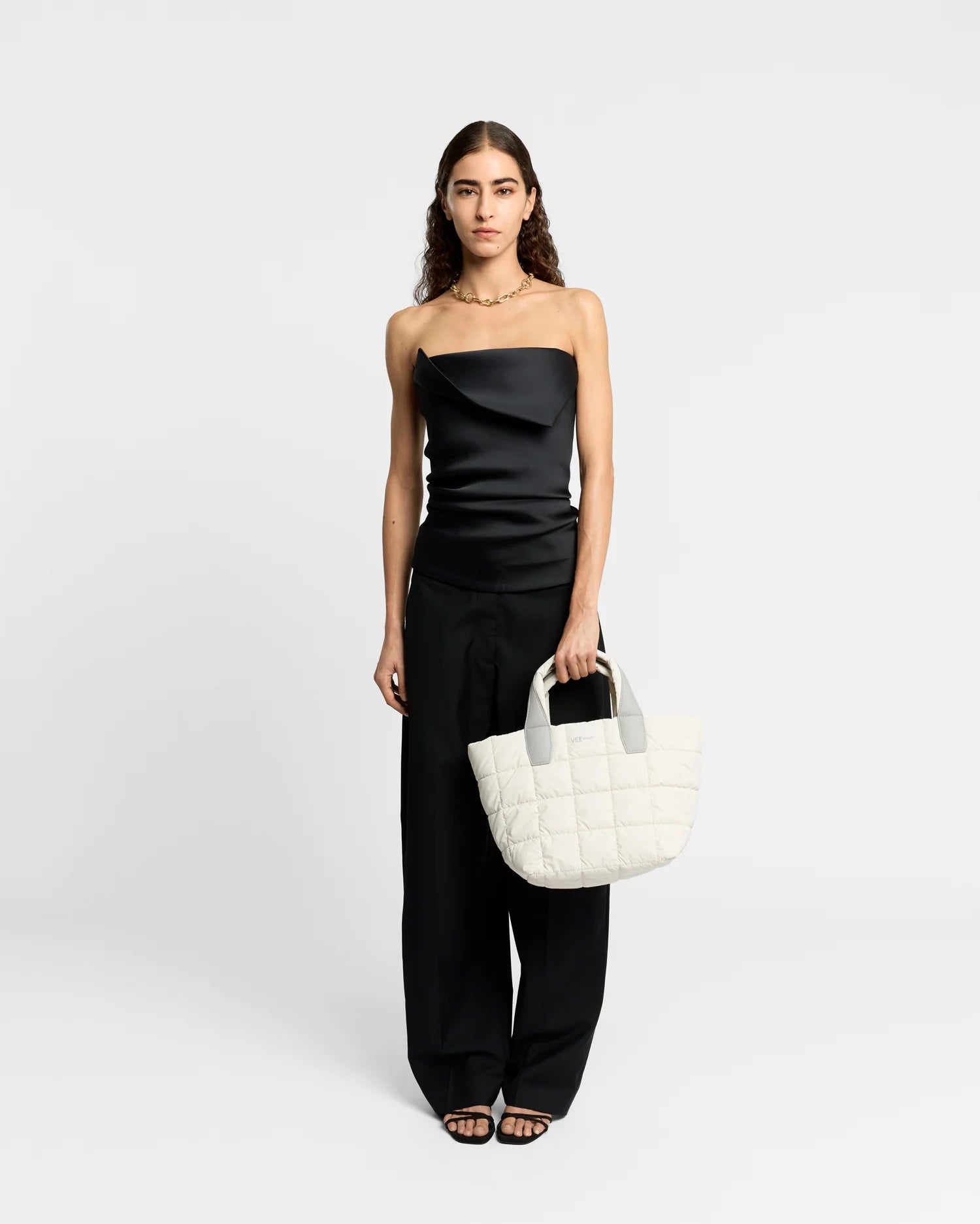 On-body picture of a woman holding the Small Porter Tote Bag in Barely Beige by Vee Collective, wearing a minimalistic outfit against a clean studio background.