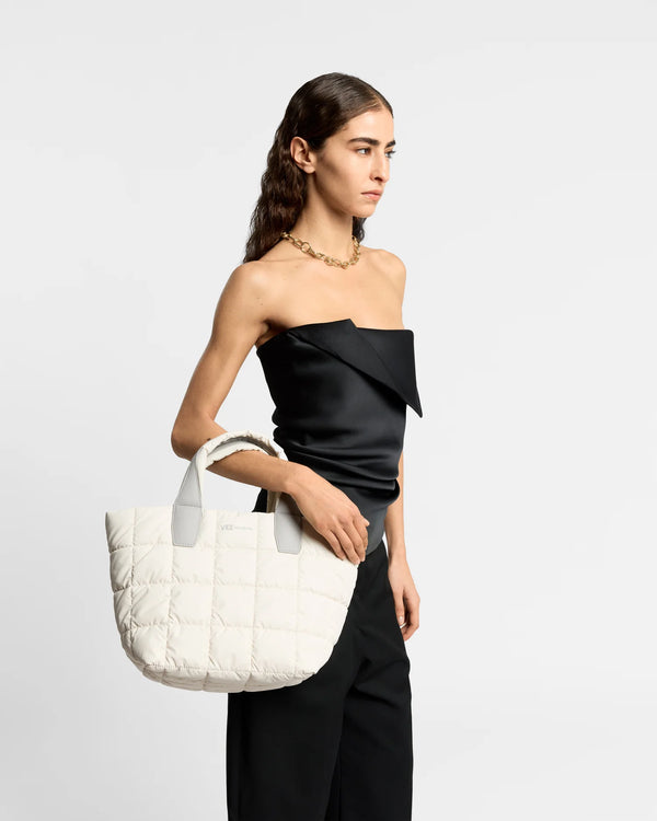 On-body picture of a woman carrying the Small Porter Tote Bag in Barely Beige by Vee Collective, wearing a minimalistic outfit against a clean studio background.