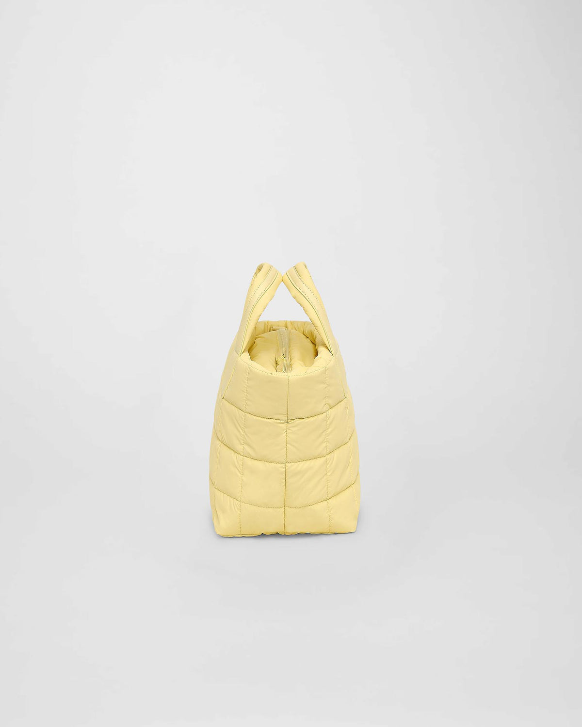 A small, quilted tote bag in a soft buttermilk yellow color is displayed against a plain background. The bag features a puffy square pattern and has two handles for easy carrying by hand or over the shoulder.
