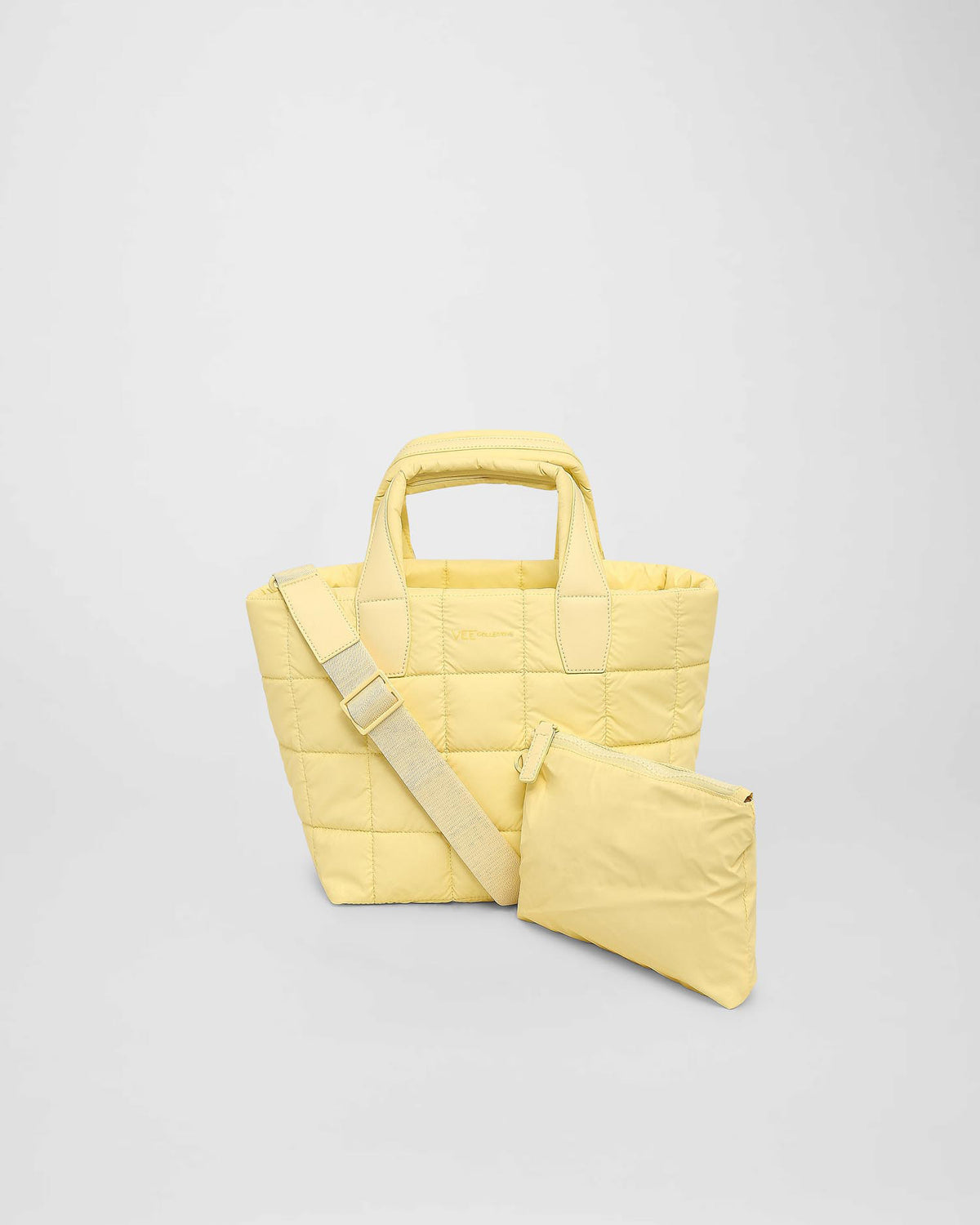 A small yellow quilted tote bag with short handles and a detachable shoulder strap is displayed, accompanied by a matching zippered pouch. The bag features a puffy square pattern, emphasizing its stylish and functional design.