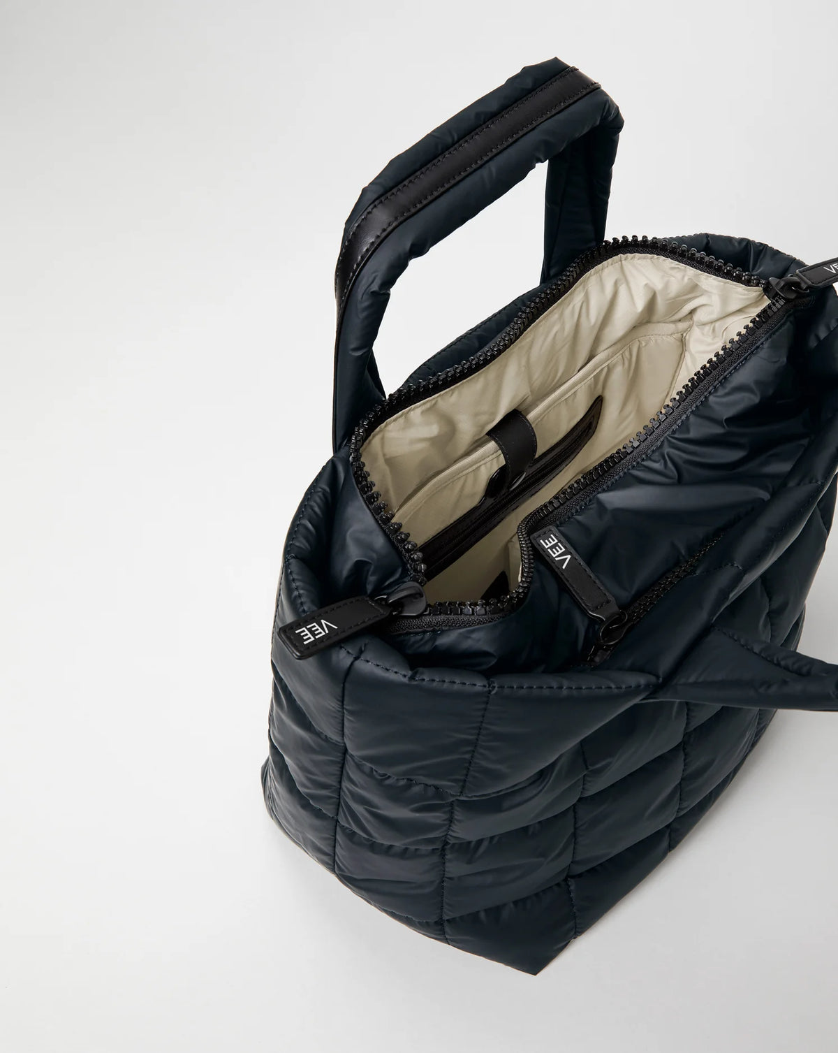 Open Vee Collective Porter Tote Bag Small in Dark Navy, showing the quilted exterior, top zipper, and interior compartments of the tote bag.