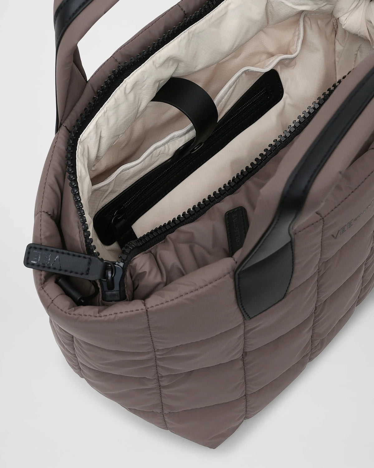 An overhead view of a small quilted tote bag in a soft mink color, showcasing its padded square pattern. The interior features a light-colored lining with a zippered pocket.