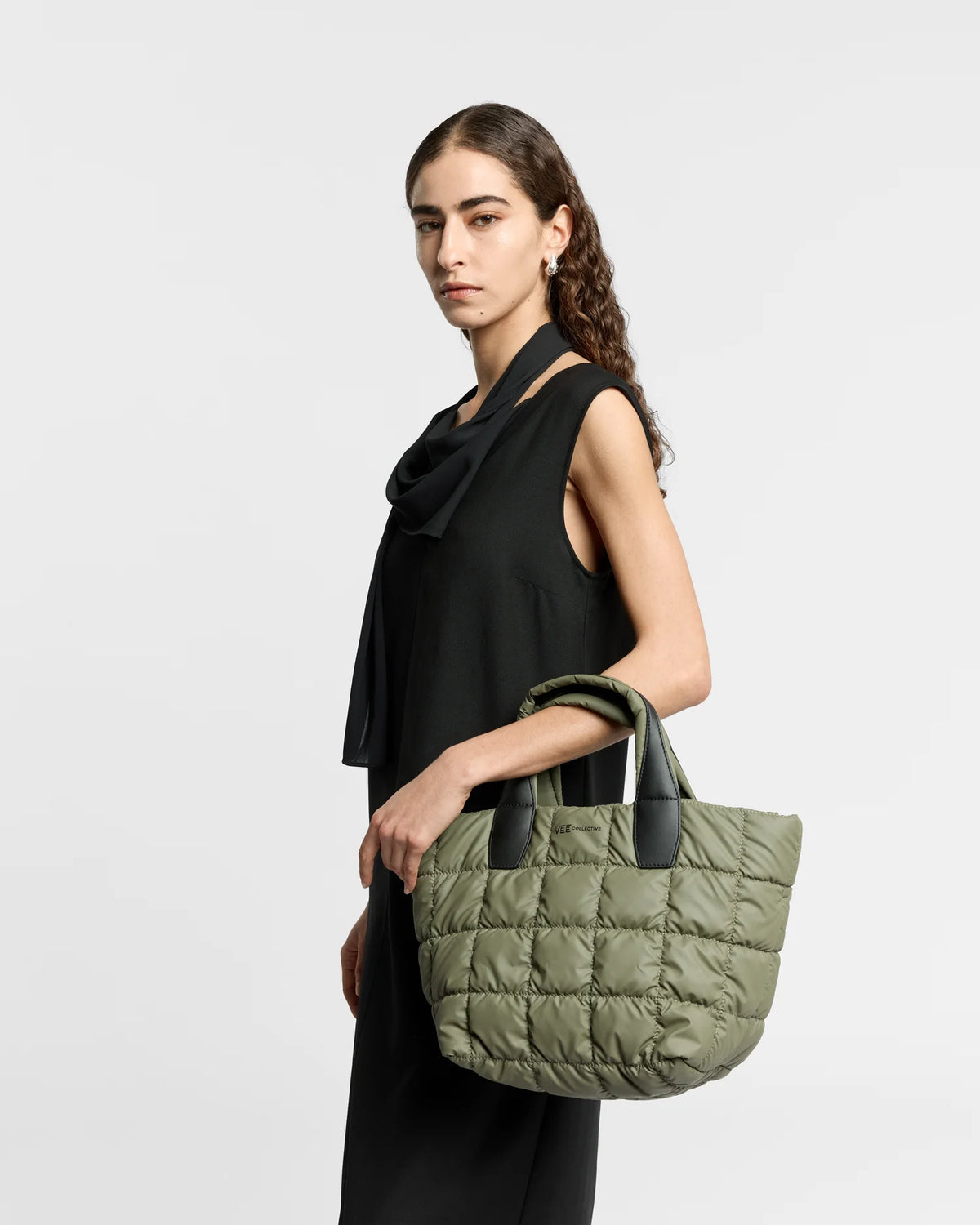 Woman wearing a clean outfit holding the Vee Collective Small Porter Tote Bag in Moss, shown in profile against a clean background.