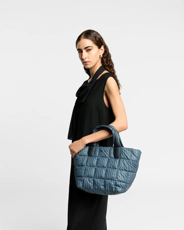 On-body picture of a woman carrying the Small Porter Tote Bag in Pinstripe by Vee Collective, wearing a minimalistic outfit against a clean studio background.