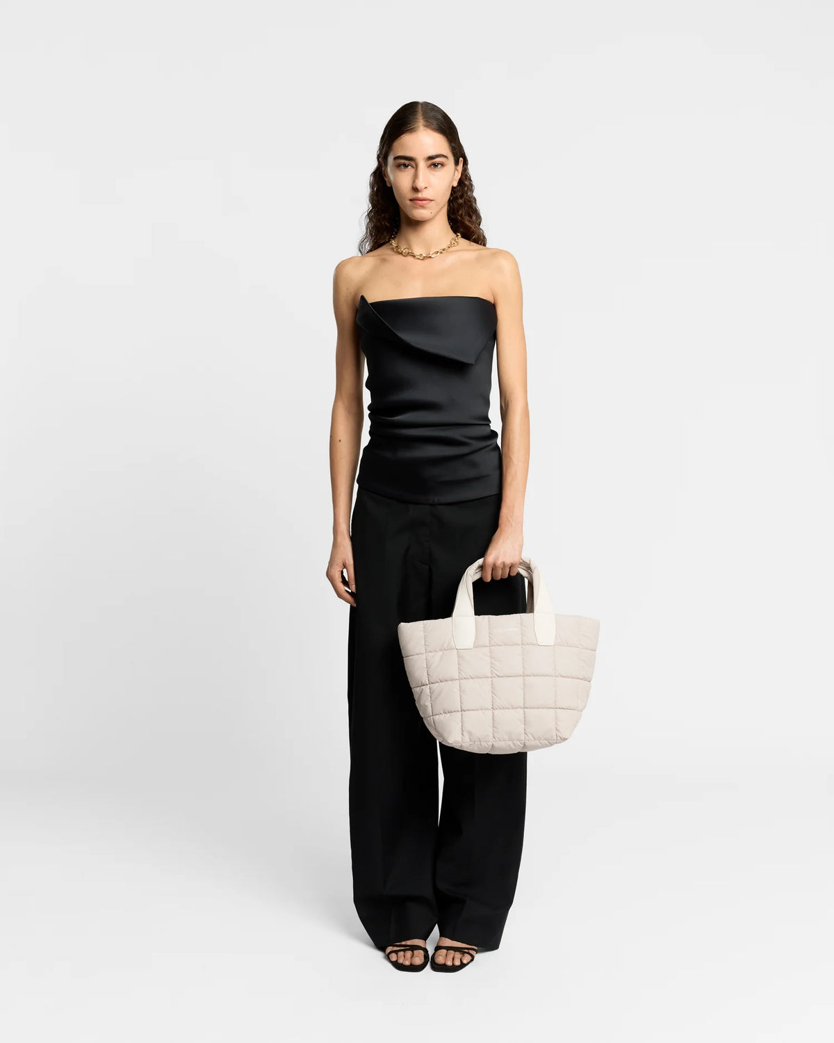 On-body picture of a woman holding the Small Porter Tote Bag in Soft Taupe by Vee Collective, wearing a minimalistic outfit against a clean studio background.