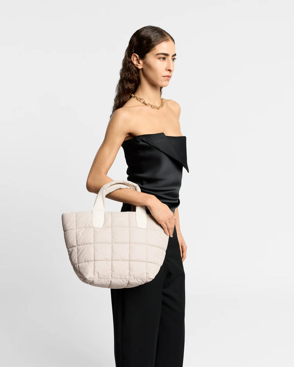 On-body picture of a woman carrying the Small Porter Tote Bag in Soft Taupe by Vee Collective, wearing a minimalistic outfit against a clean studio background.