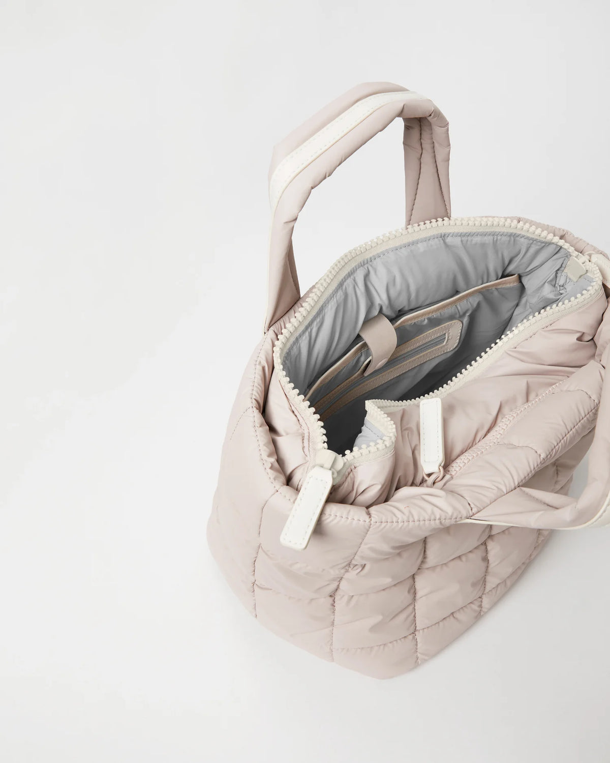 Open Vee Collective Porter Tote Bag Small in Soft Taupe, showing the quilted exterior, top zipper, and interior compartments of the tote bag.