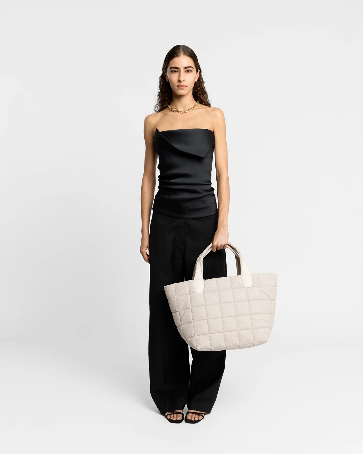 On-body picture of a woman holding the Medium Porter Tote Bag in Soft Taupe by Vee Collective, wearing a minimalistic outfit against a clean studio background.