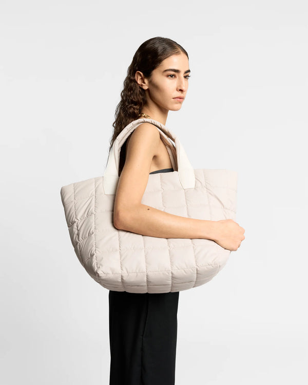 On-body picture of a woman carrying the Medium Porter Tote Bag in Soft Taupe by Vee Collective, wearing a minimalistic outfit against a clean studio background.
