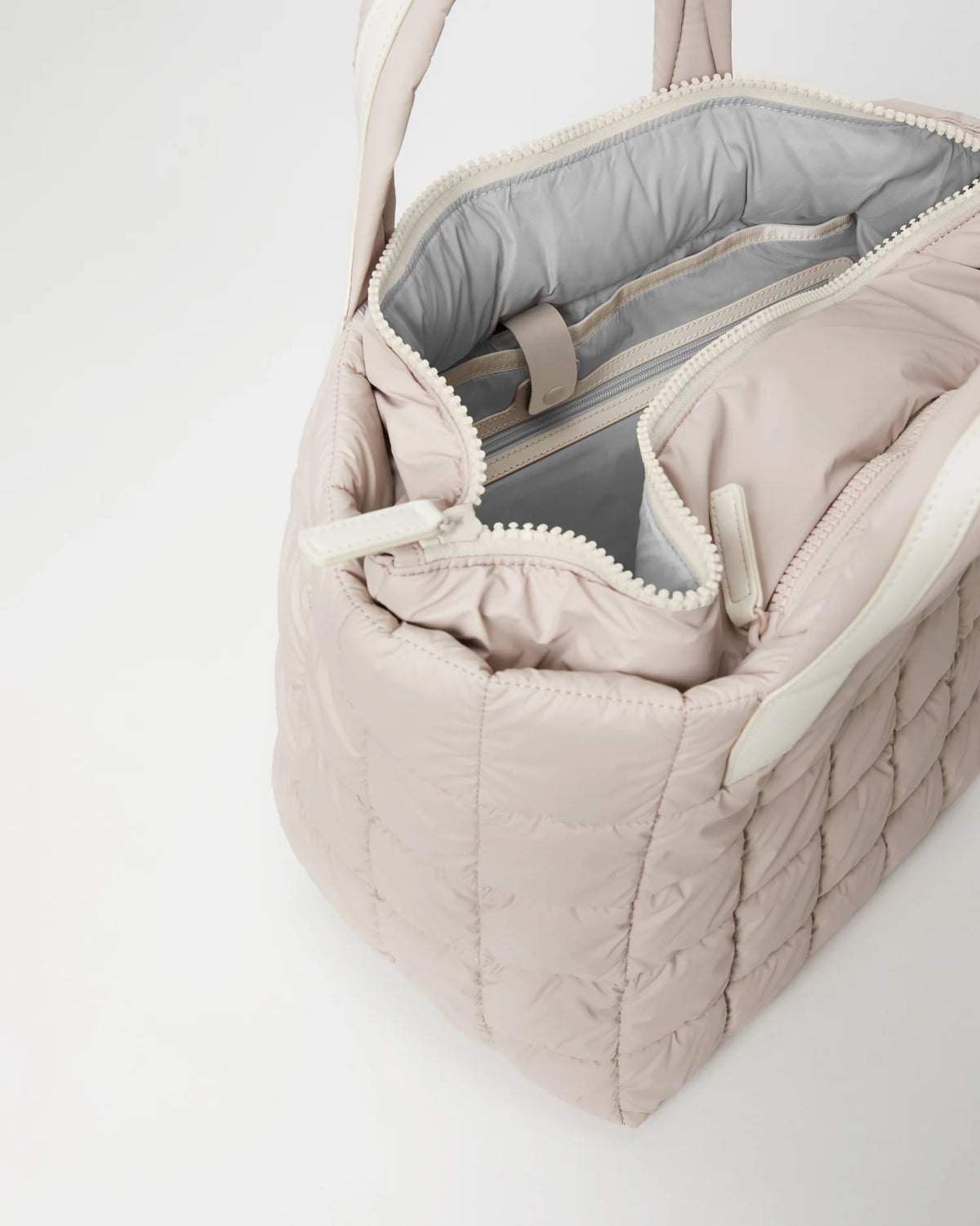 Open Vee Collective Porter Medium Tote Bag in Soft Taupe, showing the quilted exterior, top zipper, and interior compartments of the tote bag.