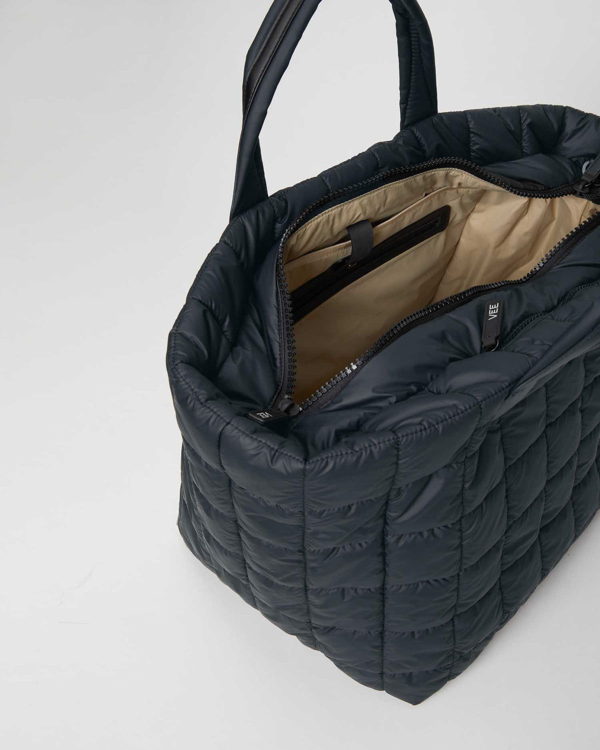 A  porter weekender bag in dark navy shown open, revealing a beige interior lining and a zippered compartment. The bag has a distinctive rounded rectangular shape with a padded, quilted texture and double top handles, photographed on a white background.