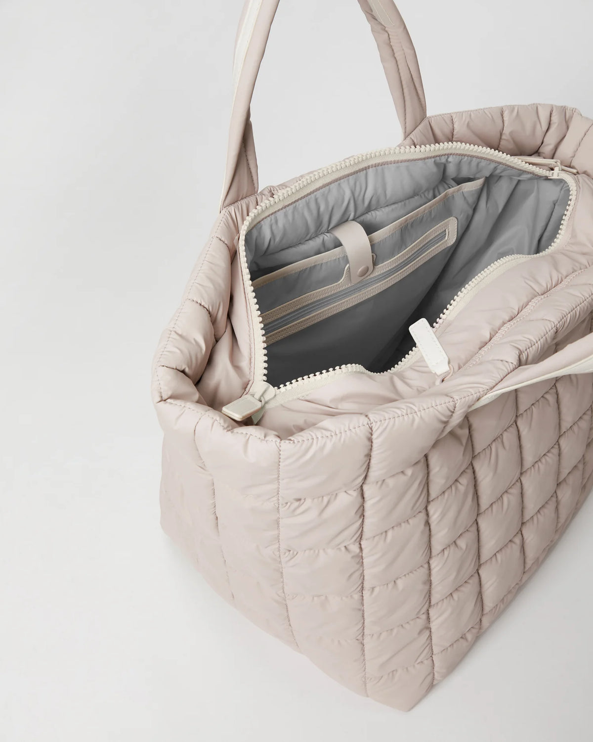 Open Vee Collective Porter Weekender Tote Bag in Soft Taupe, showing the quilted exterior, top zipper, and interior compartments of the tote bag.