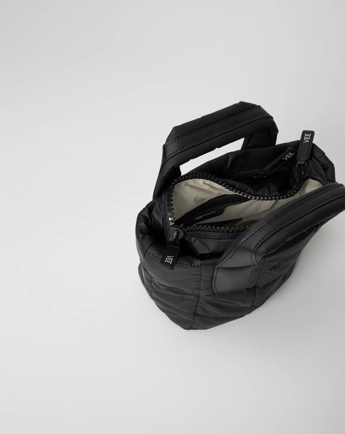 Open Vee Collective Porter Tote Mini in Matt Black, showing the quilted exterior, top zipper, and interior compartments of the tote bag.