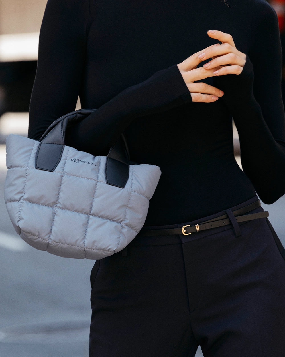 Person holding a gray quilted handbag with a blurred background
