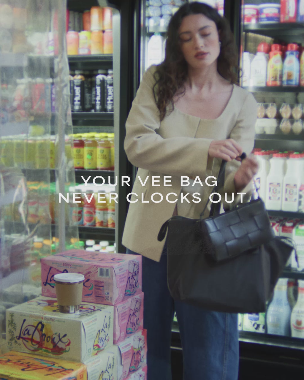 A video featuring a model in a supermarket carrying an Essence City Tote Black while picking up a cup of coffee.