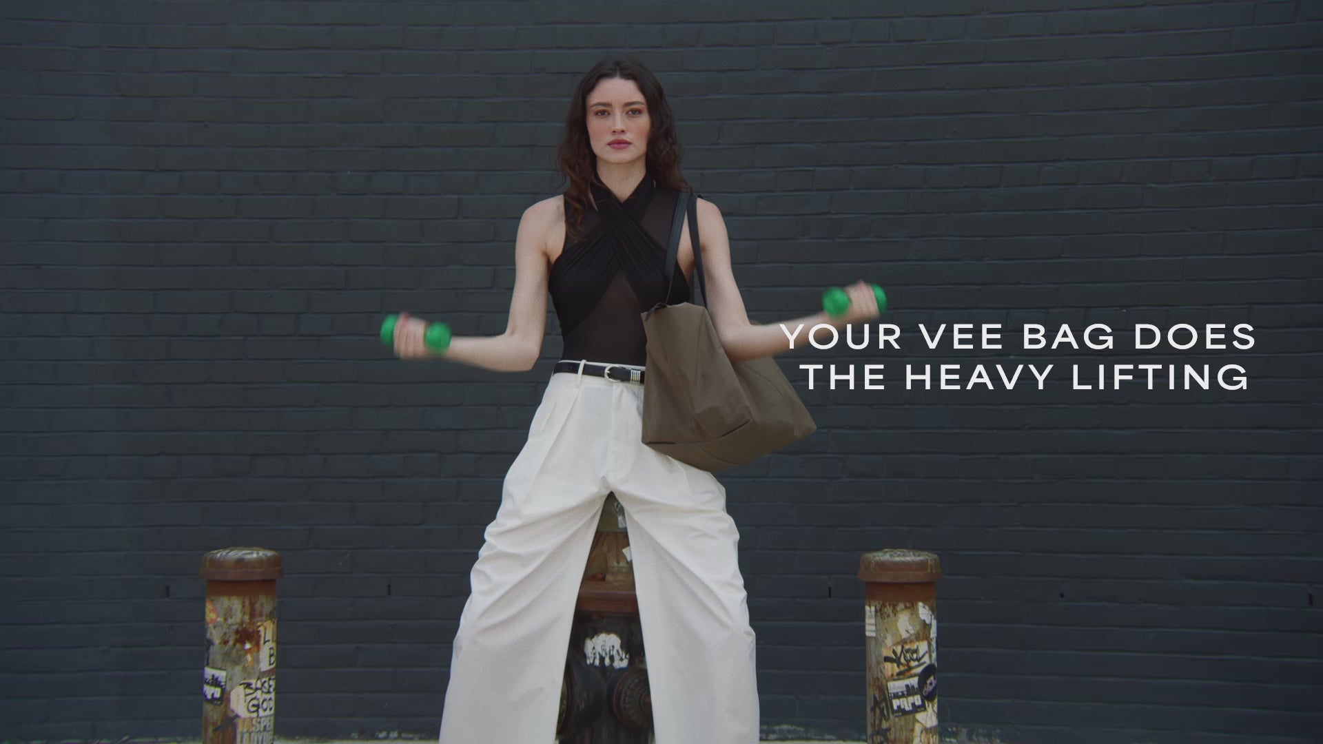 A video featuring a model wearing a sleeveless top and white trousers, carrying an Essence Medium Mink Bag while exercising with weights.
