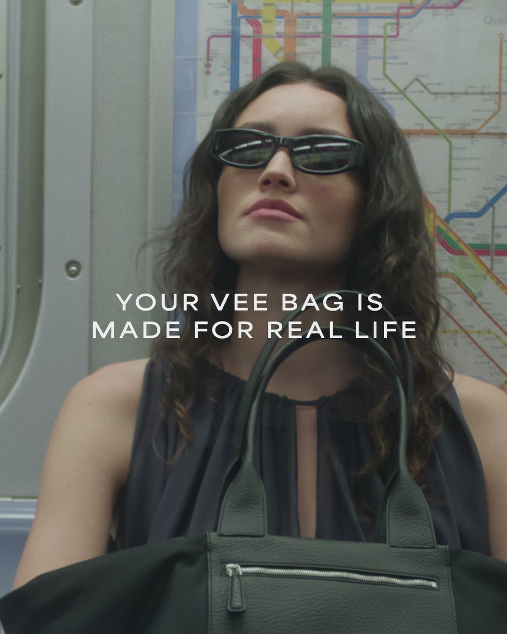 A video featuring a model wearing black sunglasses and a sheer black sleeveless top onboard a train, carrying a large black Duo tote bag with a leather handle.