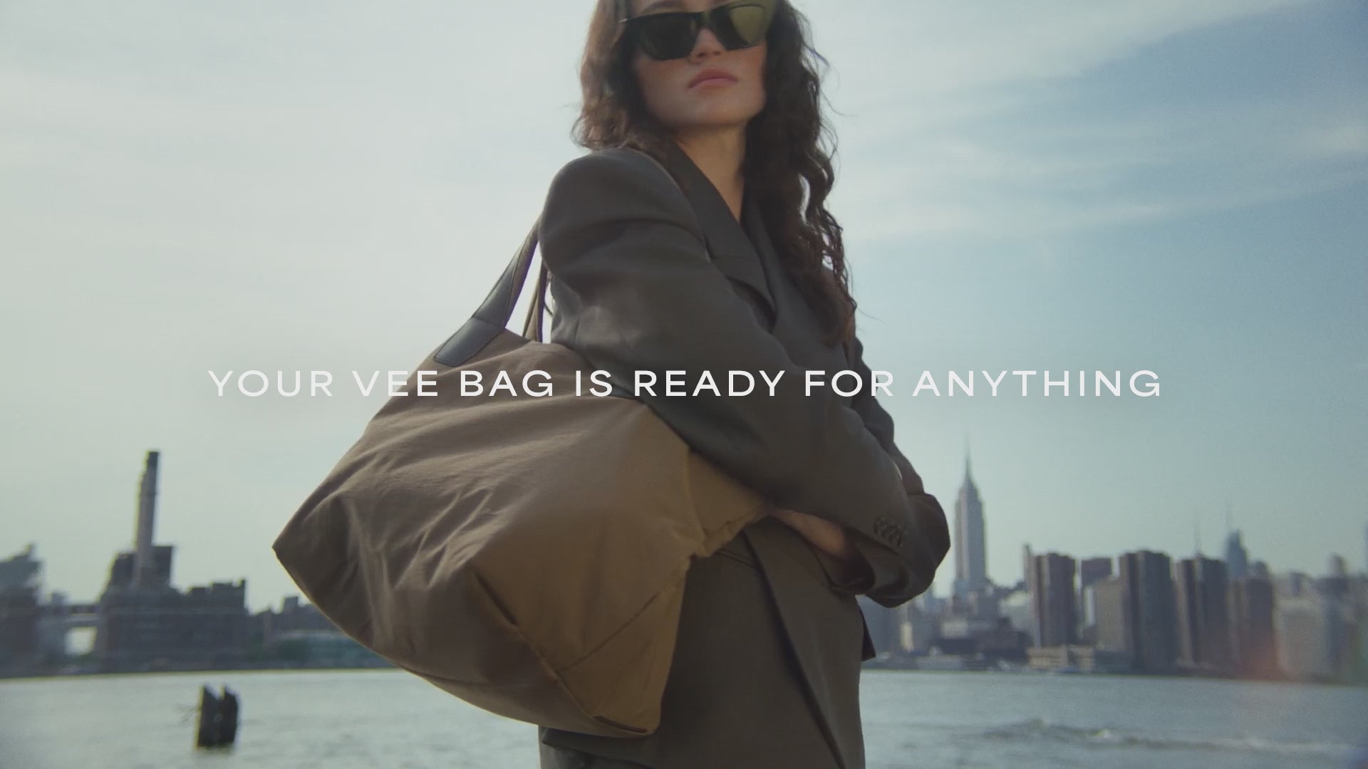 A video featuring a model wearing black sunglasses and a jacket, carrying an Essence Medium Mink Bag while standing in the city.