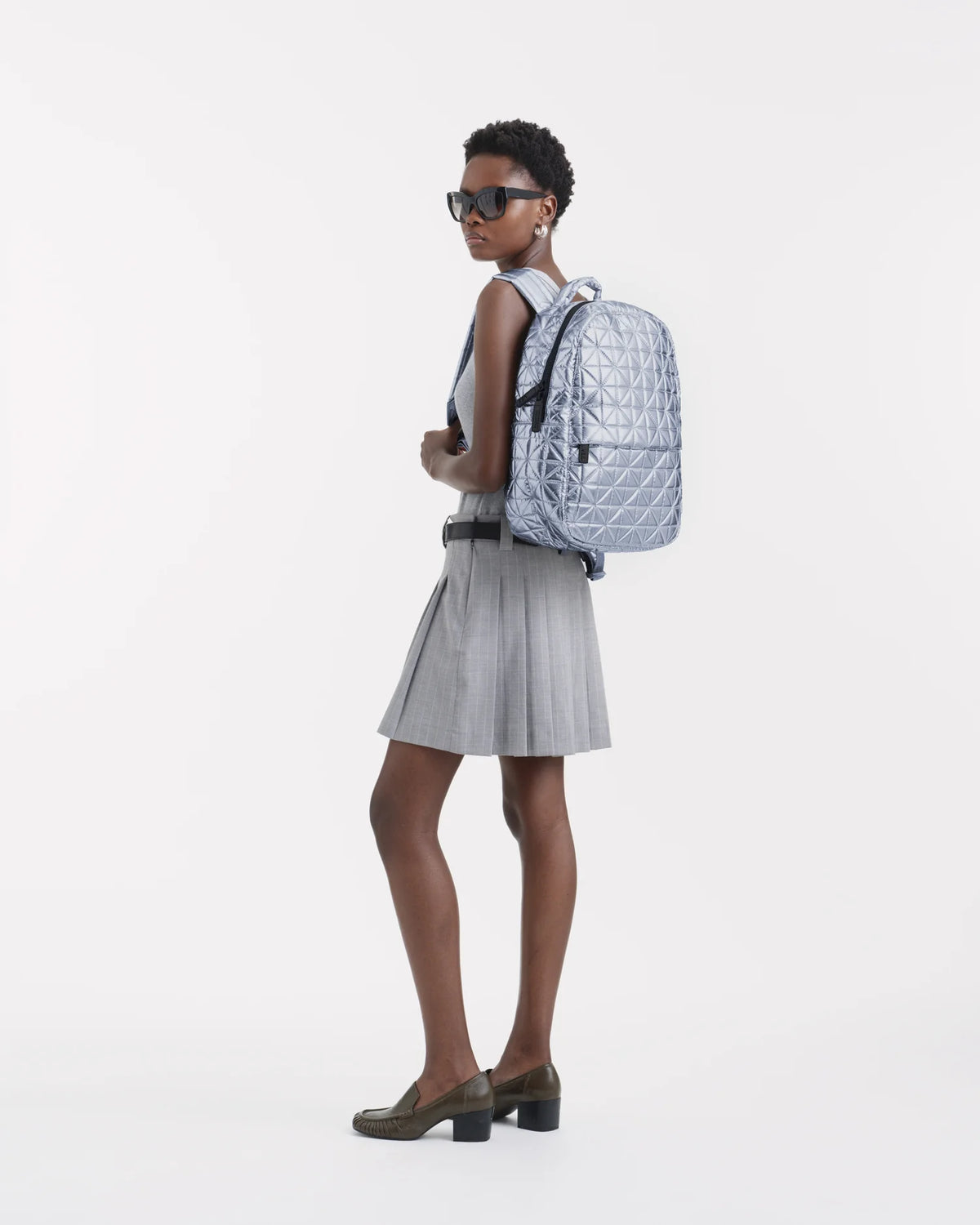 On-body picture of a woman carrying the Vee Backpack in Icy Silver by Vee Collective, wearing a minimalistic outfit against a clean studio background.