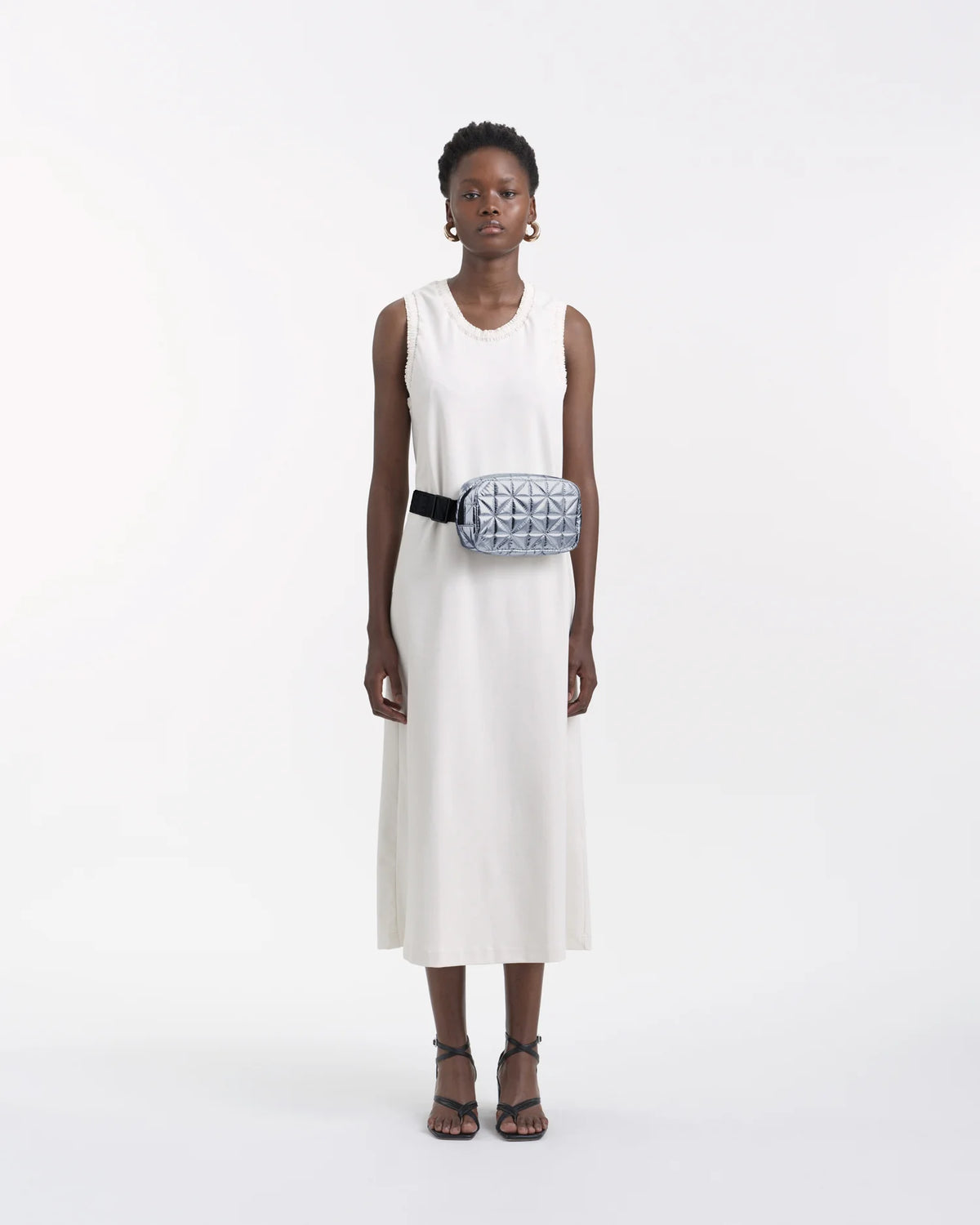 On-body picture of a woman carrying the Vee Belt Bag in Icy Silver by Vee Collective, wearing a minimalistic outfit against a clean studio background.