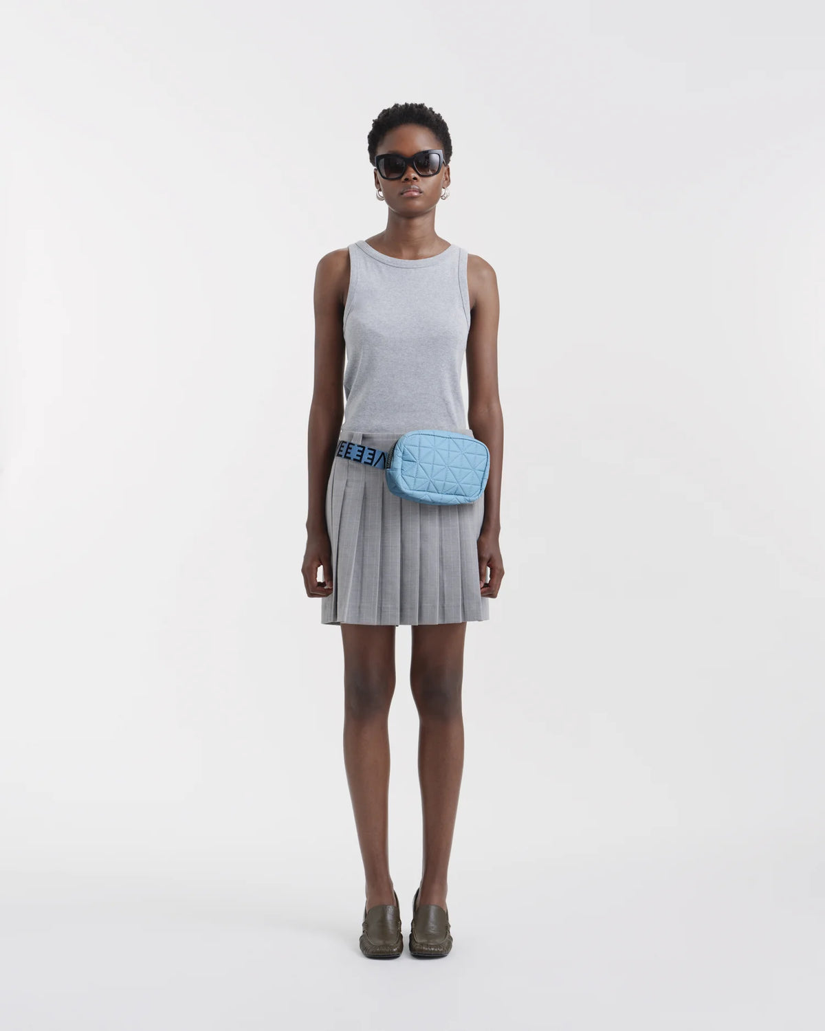 On-body picture of a woman carrying the Vee Belt Bag in Pigeon Blue by Vee Collective, wearing a minimalistic outfit against a clean studio background.
