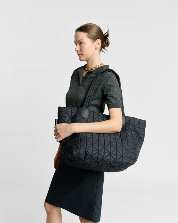 Woman wearing a clean outfit holding the Vee Collective Vee Tote Bag Medium in Black, shown in profile against a clean background.