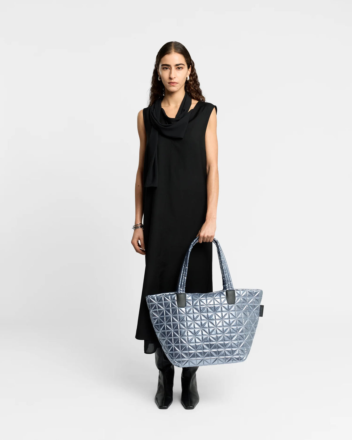 On-body picture of a woman holding the Vee Tote Bag Medium in Icy Silver by Vee Collective, wearing a minimalistic outfit against a clean studio background.