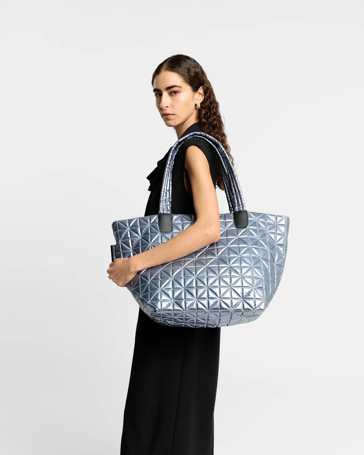 On-body picture of a woman carrying the Medium Vee Tote Bag in Icy Silver by Vee Collective, wearing a minimalistic outfit against a clean studio background.