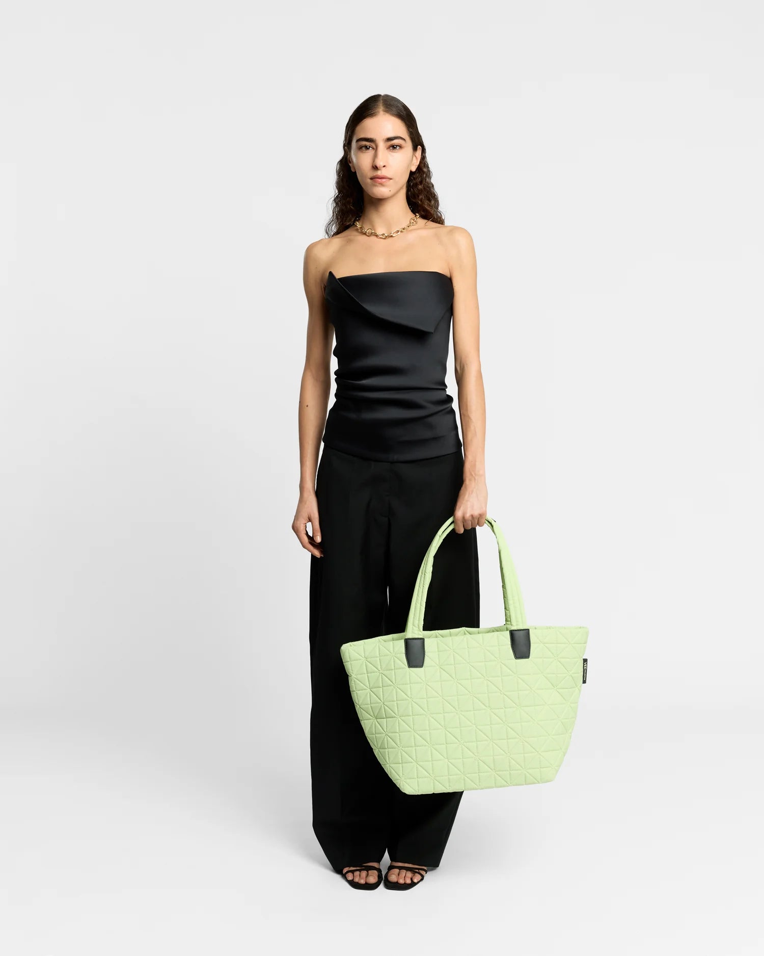 On-body picture of a woman carrying the Medium Vee Tote Bag in Limelight by Vee Collective, wearing a minimalistic outfit against a clean studio background.