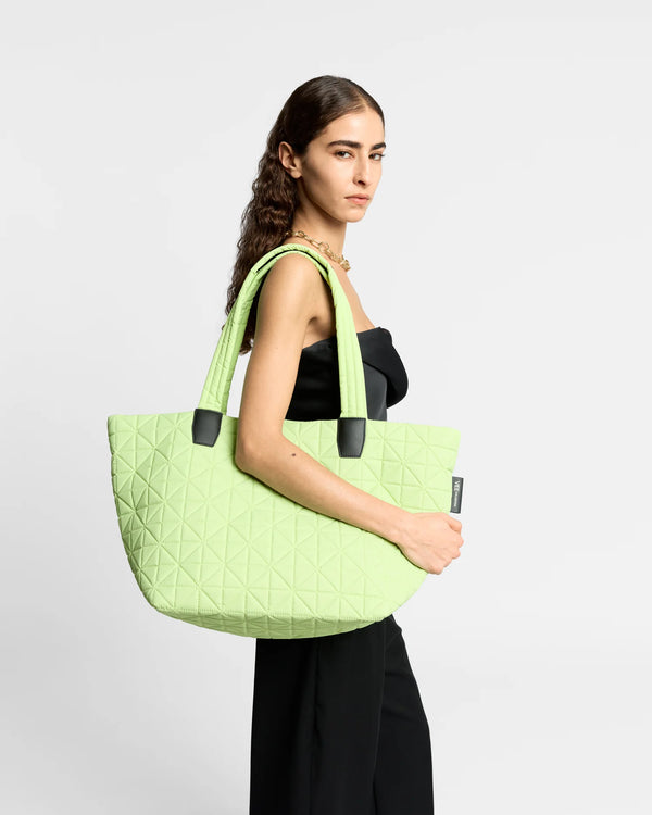 On-body picture of a woman carrying the Medium Vee Tote Bag in Limelight by Vee Collective, wearing a minimalistic outfit against a clean studio background.