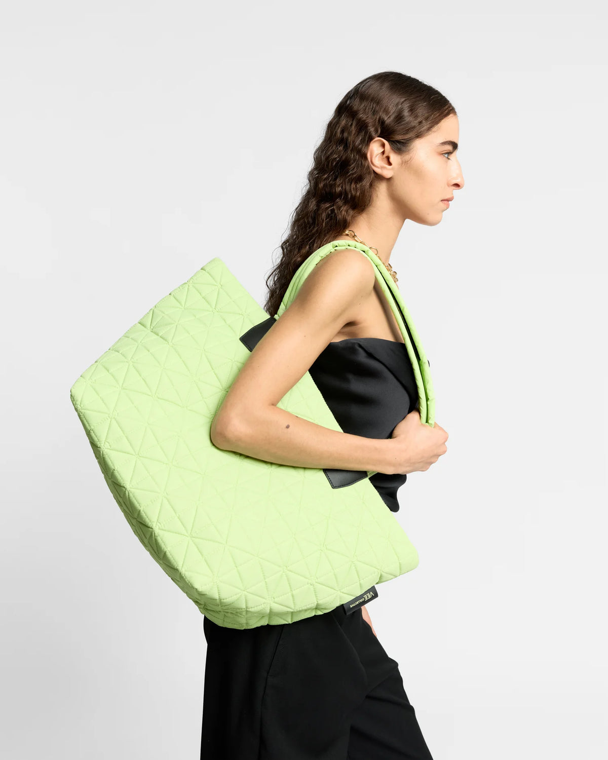 On-body picture of a woman carrying the Medium Vee Tote Bag in Limelight by Vee Collective, wearing a minimalistic outfit against a clean studio background.