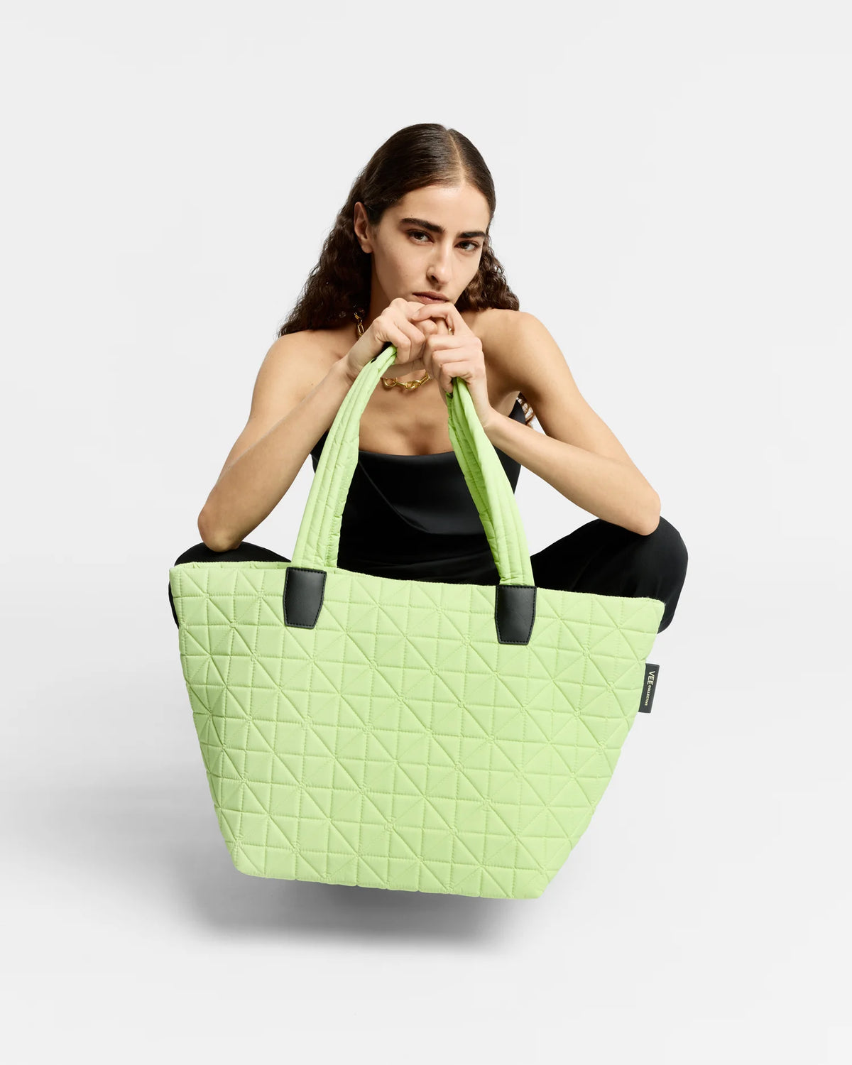 On-body picture of a woman holding the Medium Vee Tote Bag in Limelight by Vee Collective in Front of her body, wearing a minimalistic outfit against a clean studio background.