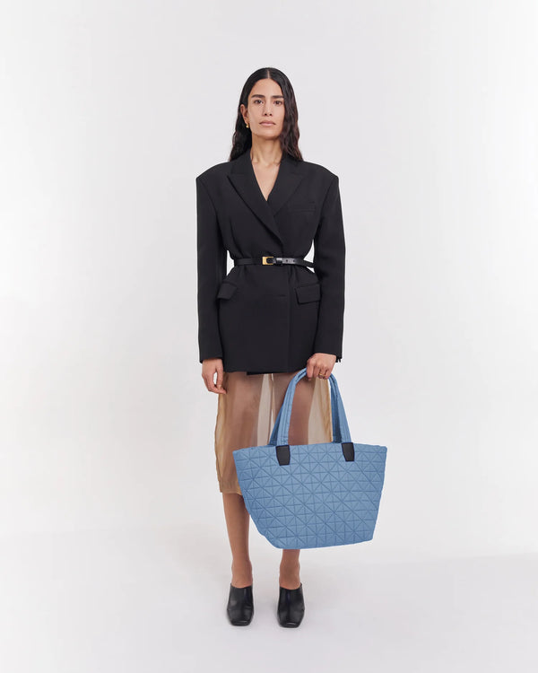 On-body picture of a woman carrying the Medium Vee Tote Bag in Pigeon Blue by Vee Collective, wearing a minimalistic outfit against a clean studio background.