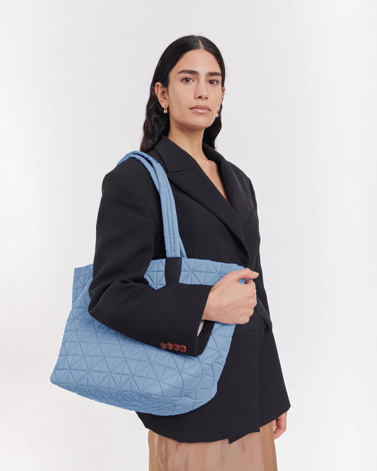 On-body picture of a woman carrying the Medium Vee Tote Bag in Pigeon Blue by Vee Collective, wearing a minimalistic outfit against a clean studio background.