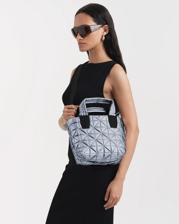 On-body picture of a woman carrying the Mini Vee Tote Bag in Icy Silver by Vee Collective Crossbody, wearing a minimalistic outfit against a clean studio background.