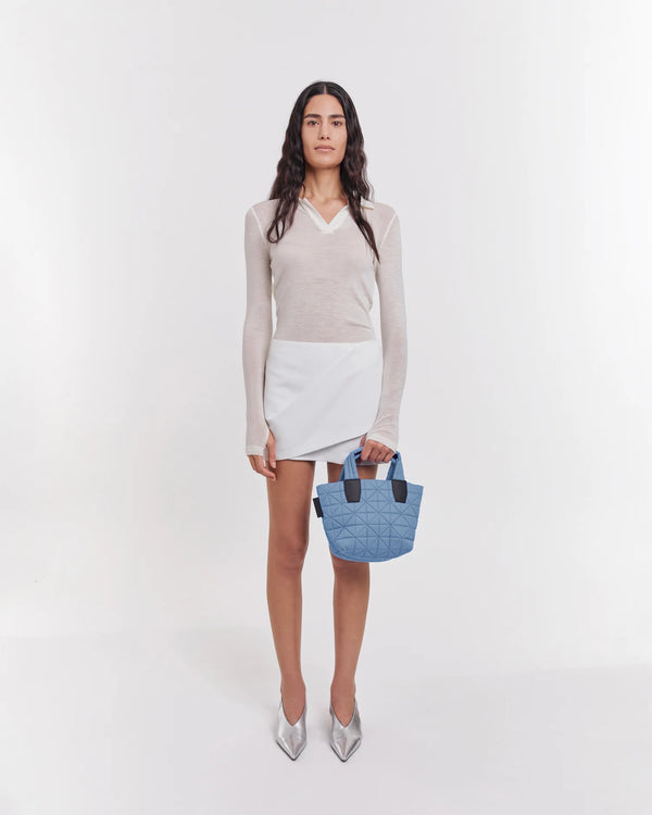 On-body picture of a woman carrying the Mini Vee Tote Bag in Pigeon Blue by Vee Collective, wearing a minimalistic outfit against a clean studio background.