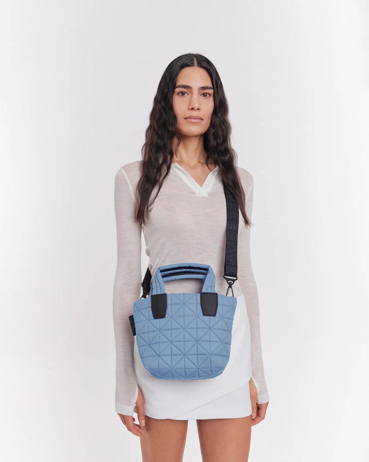 On-body picture of a woman carrying the Mini Vee Tote Bag in Pigeon Blue by Vee Collective Crossbody, wearing a minimalistic outfit against a clean studio background.