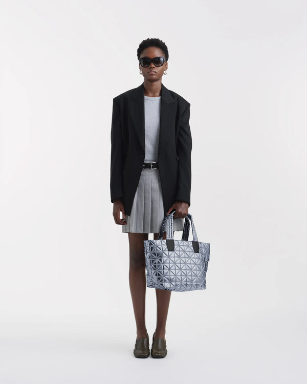 On-body picture of a woman carrying the Small Vee Tote Bag in Icy Silver by Vee Collective, wearing a minimalistic outfit against a clean studio background.