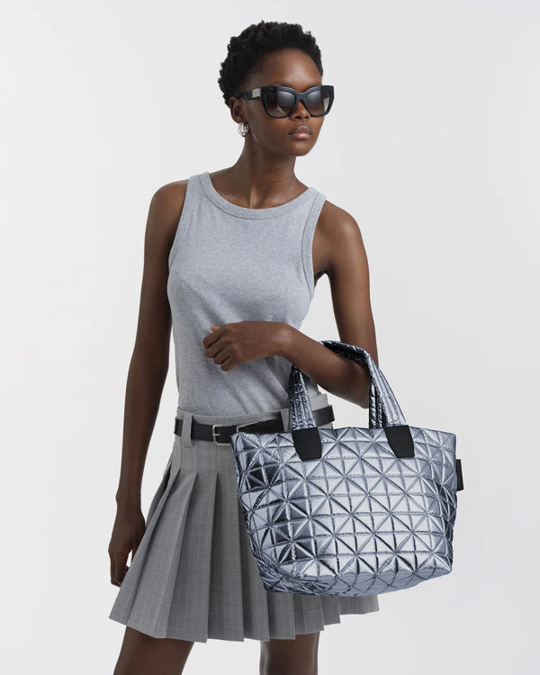 On-body picture of a woman carrying the Small Vee Tote Bag in Icy Silver by Vee Collective, wearing a minimalistic outfit against a clean studio background.
