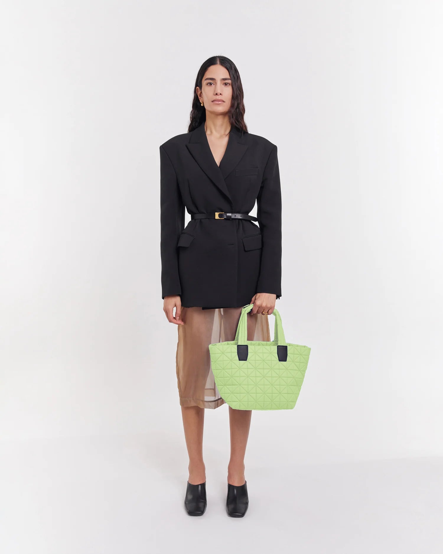 On-body picture of a woman carrying the Small Vee Tote Bag in Limelight by Vee Collective, wearing a minimalistic outfit against a clean studio background.
