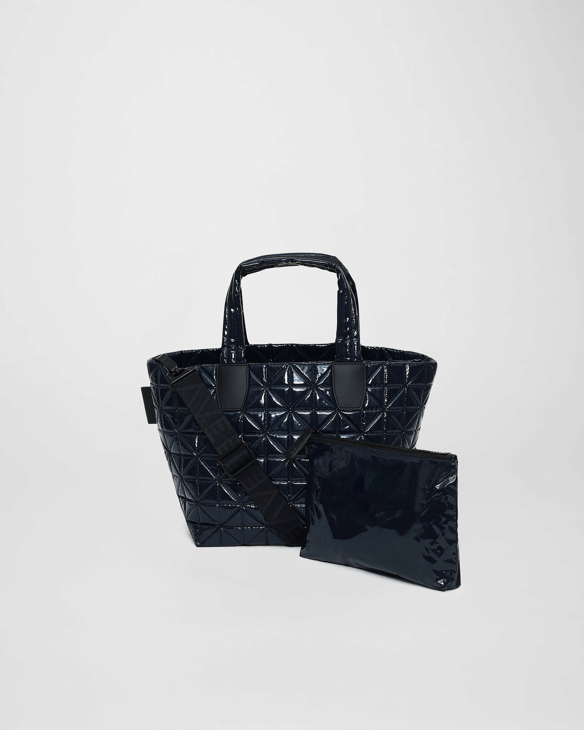 A small midnight blue tote bag features a quilted triangle design with geometric stitching. The bag includes sturdy handles and a detachable shoulder strap, accompanied by a matching, glossy pouch for added convenience.